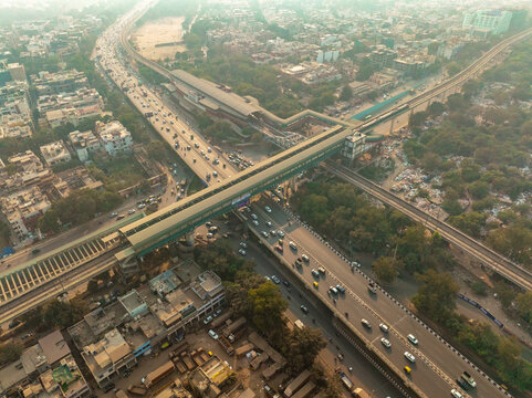 Aerial view of the elevated metro line and bustling roads contrasting with the surrounding greenery, New Delhi, Delhi, India.