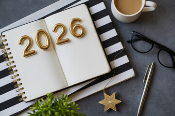 Open notebook displaying 2026 in gold numerals surrounded by coffee pen and plant representing the upcoming year and planning
