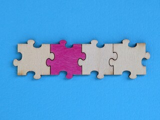Obraz premium A row of wooden puzzle pieces lies against a bright blue background, with the center piece in pink. The image conveys teamwork, collaboration and problem-solving in a modern, colorful composition