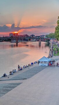 Aerial view of La Grave Hospital with Saint-Pierre Bridge. Port de la Daurade park along the Garonne River timelapse in Toulouse, France. Sunset colorful clouds, ferry at dock and riverside atmosphere