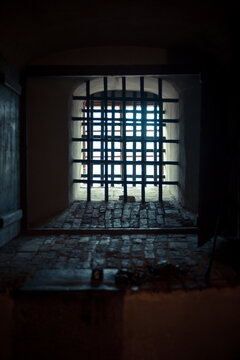 Stone prison cell inside an old medieval castle, rusty metal bars and dim light creating a dark historical atmosphere. Symbol of medieval justice and confinement.