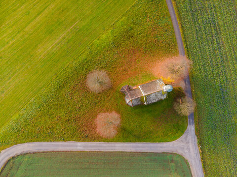 Aerial view of a quaint building embraced by autumnal trees nestled amidst vibrant green fields where Hofstatterweg meets, Raisting, Bayern, Germany.