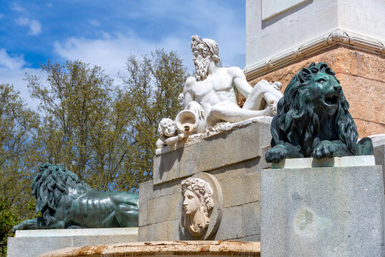 A close-up of the fountain base near the Palacio Real, showing a white marble statue of a bearded man with a cherub, flanked by bronze lion sculptures and stone carvings