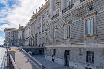 Close-up upward view of the Palacio Real’s ornate gray and white neoclassical façade, showing columns, statues, balustrade, and detailed windows against the sky