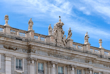 Close-up upward view of the Palacio Real’s ornate gray and white neoclassical façade, showing columns, statues, balustrade, and detailed windows against the sky