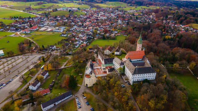 Aerial view of the Andechs Abbey complex, with its creamy walls and russet roof, nestled amongst the vibrant autumn foliage, Andechs, Bayern, Germany.