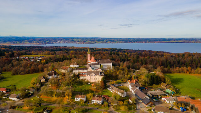 Aerial view of the Andechs Abbey stands tall against a tapestry of autumnal forests and shimmering lake waters, Andechs, Bayern, Germany.
