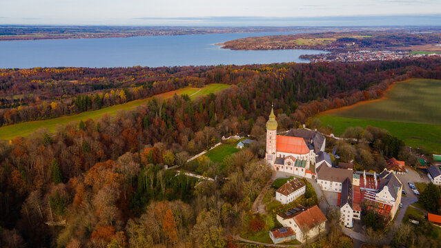 Aerial view of a serene church nestled among golden autumn trees, with a vast lake stretching to the horizon, Andechs, Bavaria, Germany.