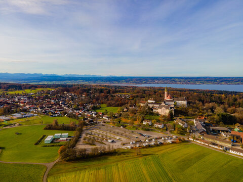 Aerial view of the Andechs Abbey complex standing majestically amid a tapestry of golden autumn foliage and vibrant green fields, Andechs, Bayern, Germany.
