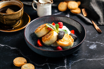 Traditional Russian syrniki served with whipped cream, strawberries, raspberries and blackberries on dark marble table