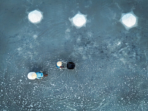 Ninh Hoa, Vietnam - 24 June 2025: Aerial view of workers in the water harvesting salt under the intense sun, creating a mesmerizing dance of light and shadow on the water surface.