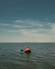 A trip across the water with a loyal friend. A man and a dog in a red inflatable kayak against the background of an endless blue horizon and cloudy sky. Peace and adventure.