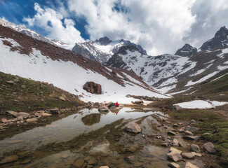 A crystal clear glacial, moraine lake located in the high-altitude circus of the Trans-Ili Alatau among snow-capped peaks, reflecting the harsh mountain landscape in cold water.