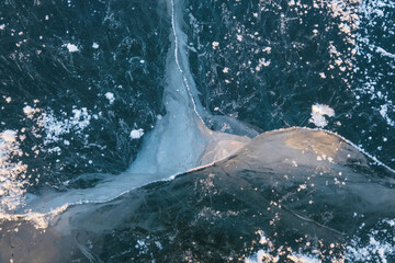 A natural wonder: a deep crack in the ice of a frozen lake. A close-up of an icy surface where blue transparent ice meets white snow and turquoise faults