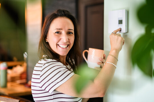 Beautiful happy woman push button digital thermostat at house