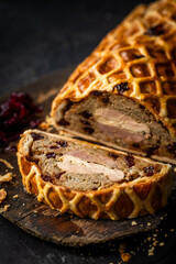 A luxurious Three Bird Wellington featuring layers of turkey, duck, and pheasant wrapped in golden puff pastry with herbed stuffing. Sliced to reveal the colourful cross-section and served on a rustic