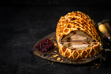 A luxurious Three Bird Wellington featuring layers of turkey, duck, and pheasant wrapped in golden puff pastry with herbed stuffing. Sliced to reveal the colourful cross-section and served on a rustic