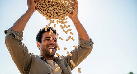 Happy young man pouring a basket of peanuts over his head outdoors. Joyful farmer celebrating a successful harvest. Agriculture and abundance concept with copy space