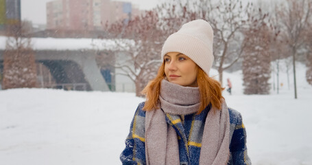 In a serene park blanketed in snow, a woman stands thoughtfully, taking in the beauty of the snowfall. Warmly dressed, she reflects amid the winter wonderland.
