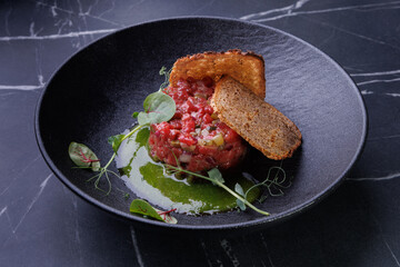 Classic beef tartare plated with toast, garnished with egg yolk and greens, emphasizing freshness and vibrant presentation.