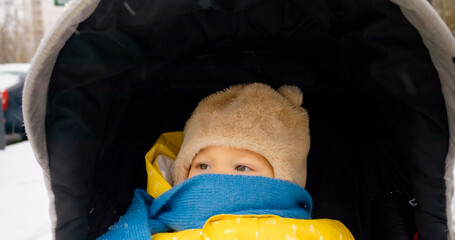 A little boy wraps himself in a scarf, wearing warm clothes as he enjoys a peaceful sleep in his stroller during a snowy winter day outdoors.