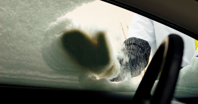 In cold weather, a woman shows determination as she clears snow from her car on a winter day. This difficult task highlights the challenges of cold climates.