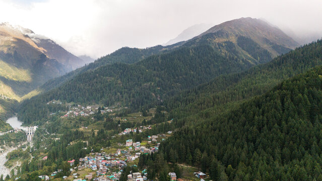 Pulga and Kalga villages in Parvati Valley, Himachal Pradesh, showing the lush green Fairy Forest with pine and deodar trees, snow-capped mountains, and clouds touching the peaks in autumn.
