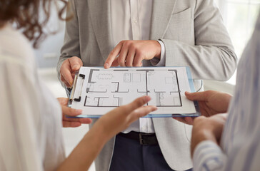 Closeup of man architect or designer showing blueprint to a young couple with design project or repair of new apartment. Meeting with foreman about interior decoration. Moving concept.