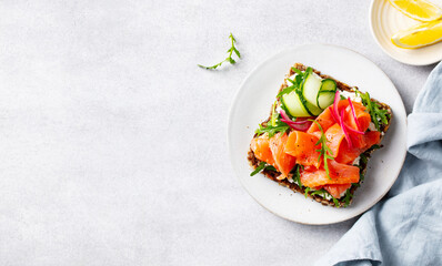 Salmon sandwich, toast with fresh cucumber, cream cheese and arugula salad on a white plate. Copy space. Top view.