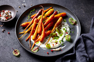 Roasted Carrots with Yogurt and North African Spices. Dark grey background. Close up.