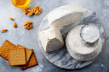 Soft cheese wheels with crackers, walnuts and honey on a marble serving board. Grey background. Top view.