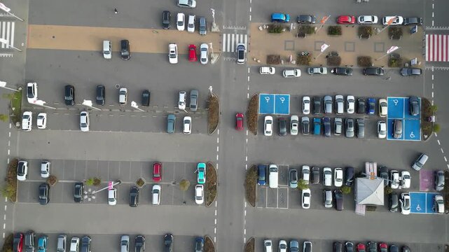 Aerial view of busy parking lot near shopping center, showcasing various parked vehicles, camera pans across scene highlighting parking dynamics and space utilization