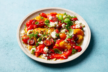 Fresh Mediterranean salad with cherry tomatoes, bell peppers, feta and herbs. Blue background. Close up.