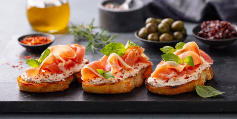 Bruschetta with jamon, creamy cheese and fresh basil leaves. Grey background. Close up.