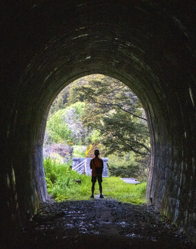 View of a lone figure silhouetted at the end of a dark tunnel, opening onto a world of vibrant greens and natural light, Kawatiri, Nelson, New Zealand.