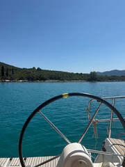 View from a sailboat helm across tranquil turquoise waters to a lush green island