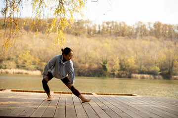 Korean woman practicing yoga by the calm lake during a serene autumn morning