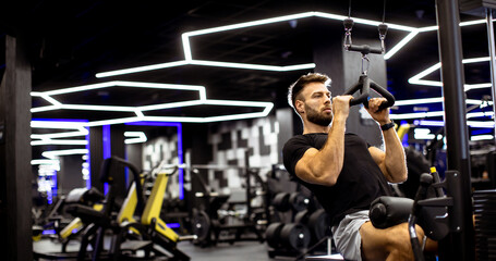 Man exercising on pull-up machine in modern gym with bright neon lights