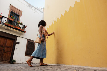 Woman touching yellow wall walking in town alley