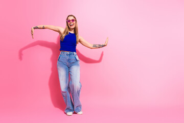 Young woman dancing in a bright pink studio wearing a blue top jeans and sunglass for a vibrant fashion lifestyle shot