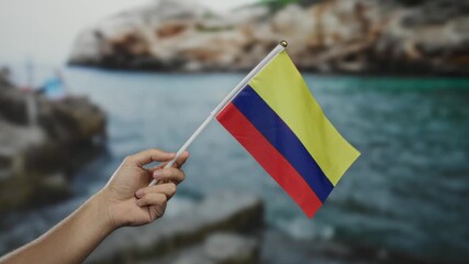 Hand of a man holding the colombian flag by the seaside, showcasing national pride in a vibrant beach setting. - Powered by Adobe