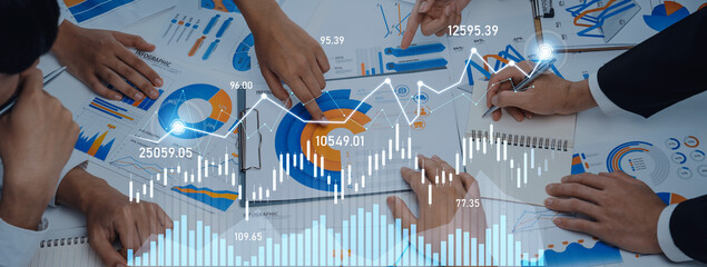 A dynamic business meeting scene showing hands of professionals working on financial graphs and...