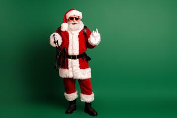 Santa Claus in a bright red costume with white fur trim and sunglass worn stands with a bag and chain on a green background for a festive Christmas campaign