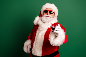 Santa with red sunglasses and a glass in a festive red suit stands against a green background ready for holiday fun and merry celebration