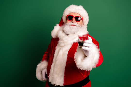 Santa with red sunglasses and a glass in a festive red suit stands against a green background ready for holiday fun and merry celebration