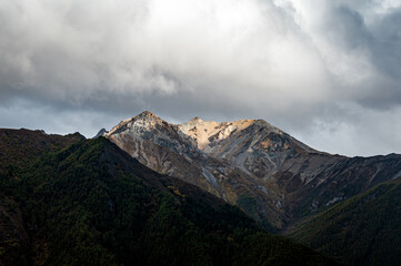 A high-altitude rocky mountain peak is partially illuminated by sunlight in the plateau mountainous area