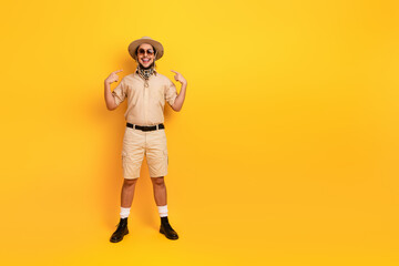 Young man in safari outfit poses against a bright yellow background for adventure travel style