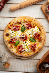 Freshly baked Italian pizza with prosciutto, burrata cheese and basil leaves on wooden board