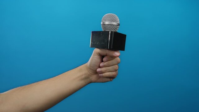 Man holding microphone against blue background, showcasing a presentation or interview setting with focus on communication and media.