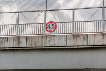 A height warning sign hanging from the metal railings of a bridge on the highway. A traffic sign indicating that the bridge height is 4.80 m.